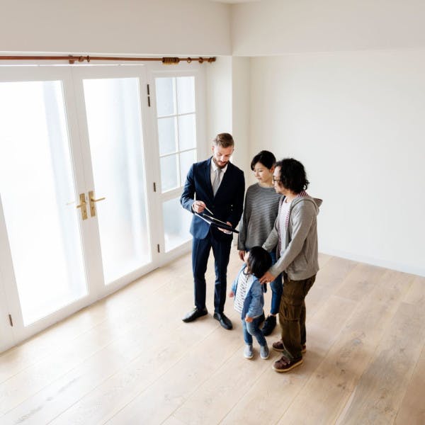 A young Asian couple and their toddler look over paperwork with their real estate agent in an empty house