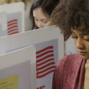 A young African American woman fills out her ballot in a voting booth