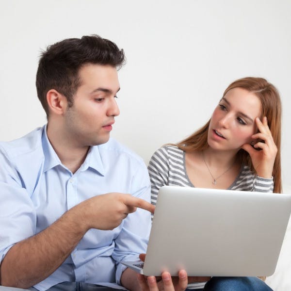 A young couple looks at a laptop with concern.