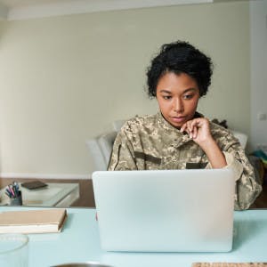A woman in a military uniform works on a laptop