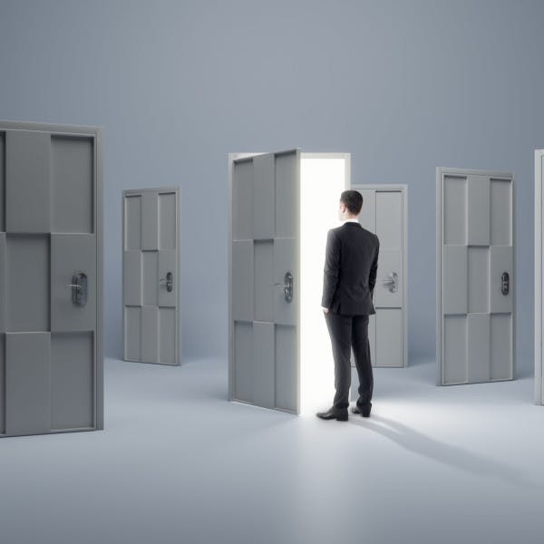 A businessman looks through an open door in a room full of doors