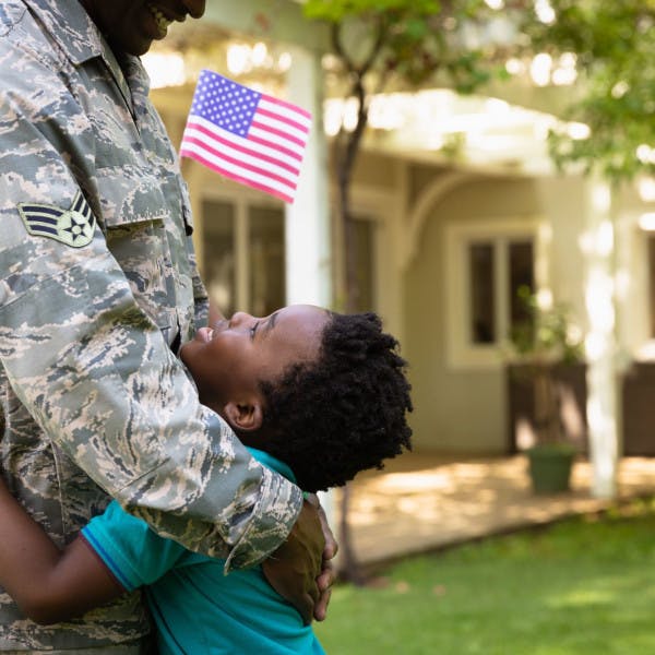A soldier hugs his young child in front of their home
