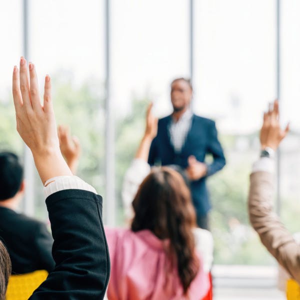 Business people raise their hands during a presentation by a Black professional