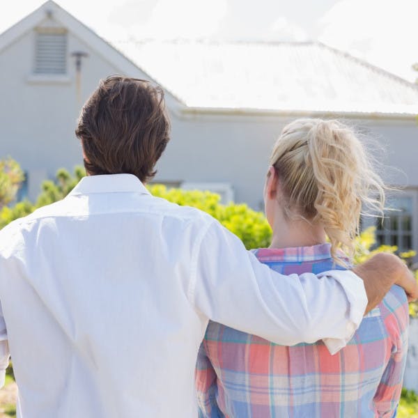 A young couple stands in a yard looking at a house for sale