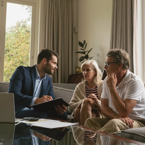 A middle-aged couple sits on the couch and discusses home-selling strategies with their real estate agent.