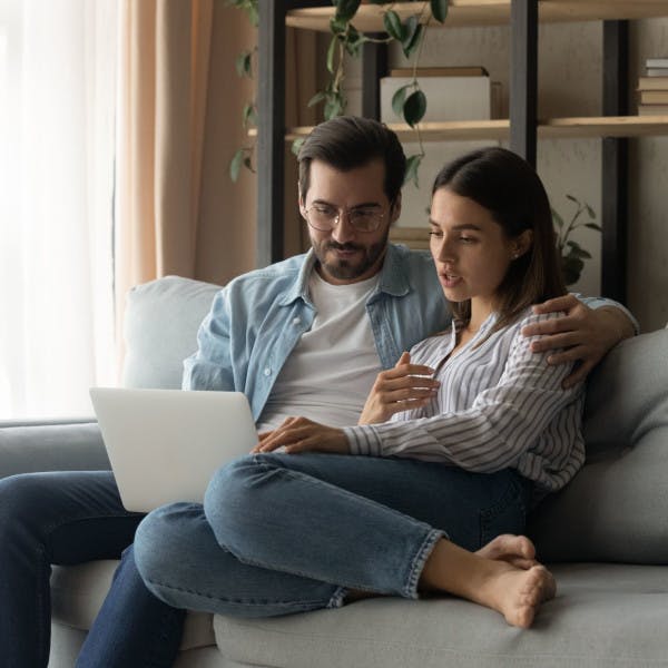 A young couple sitting on the couch looking at a laptop together