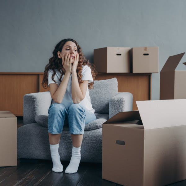 A woman sits in her apartment with moving boxes feeling tired and frustrated