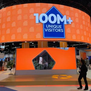 A Homes.com conference booth screen with "100M+ unique visitors"