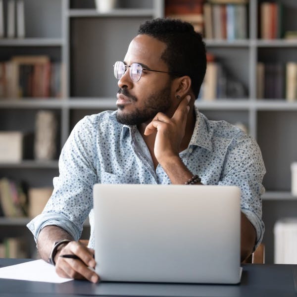 A Black businessman works at his desk with a look of contemplation and uncertainty