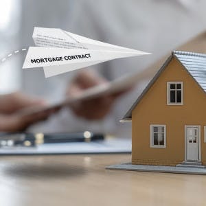 Paper plane with words mortgage contract flying over model of house