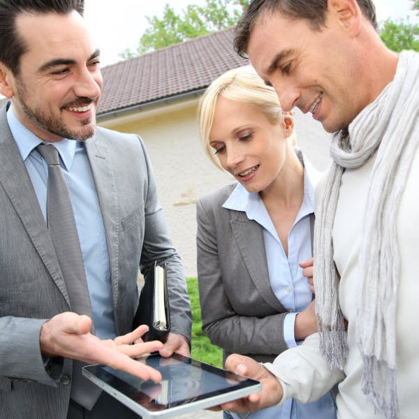 A real estate agent shows a middle-aged couple a home on a tablet