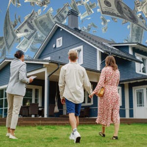 A couple and a real estate agent look at a house as money rains down from the sky.